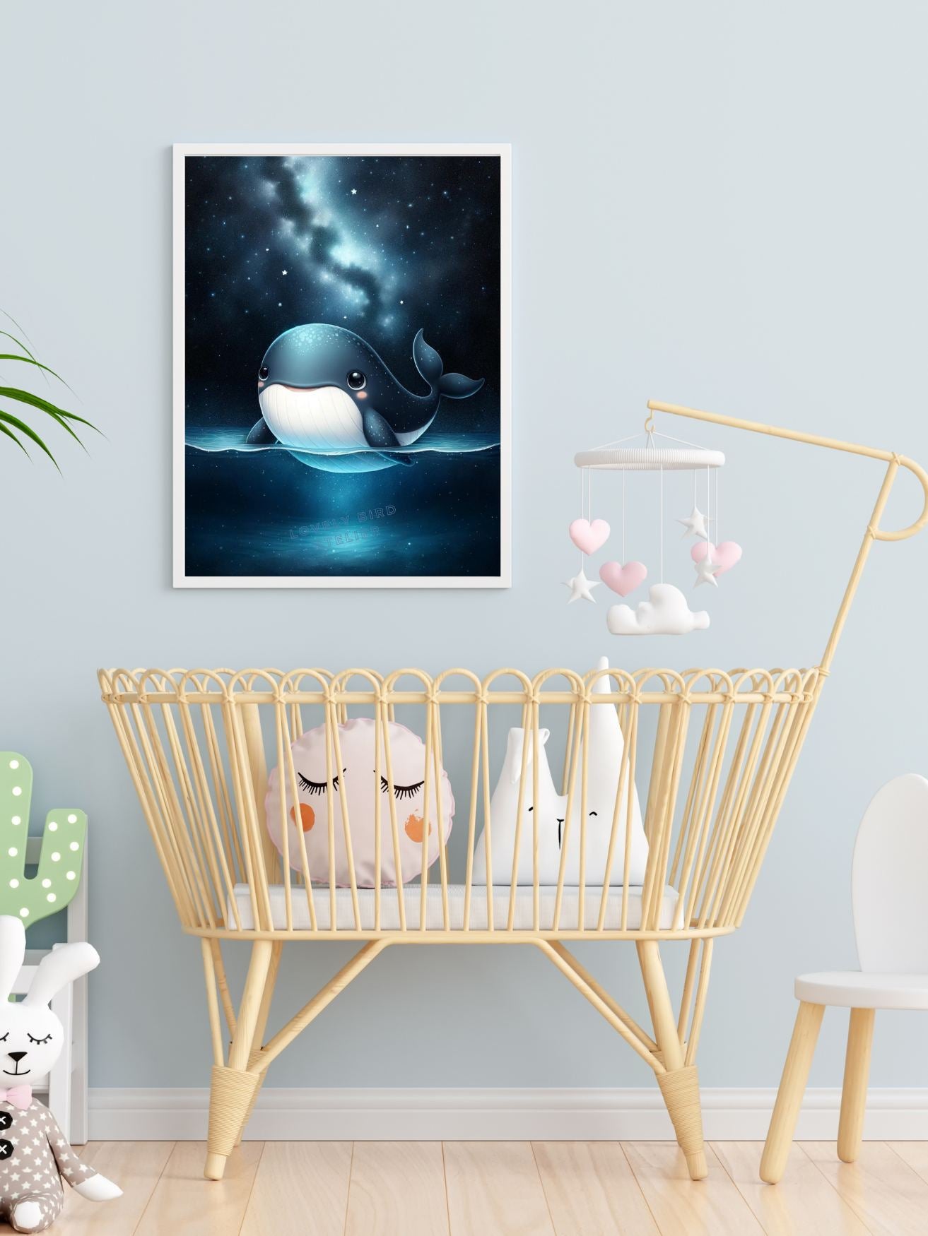 Affiche baleine douce dans chambre de bébé avec berceau en osier et mobile coloré.